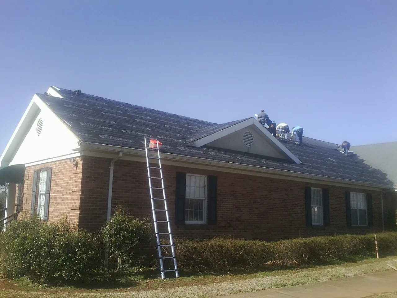 Crew tearing shingles off a brick ranch roof with a ladder set — Emergency Roof Repair work by our crew in Gauley Bridge