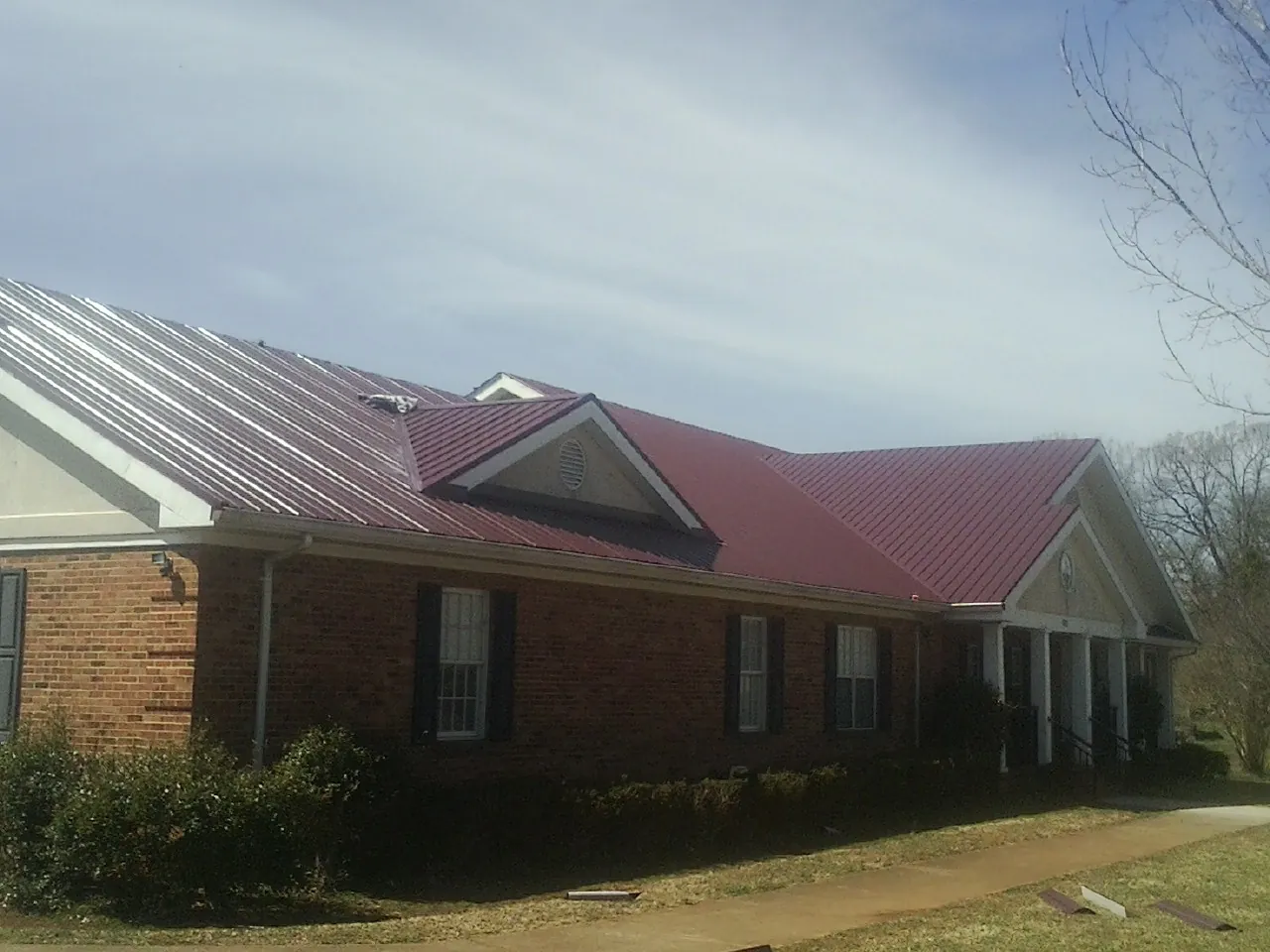 Red metal roof with gabled entries on a long brick building, from a Hail Damage Roof Repair job in Gauley Bridge
