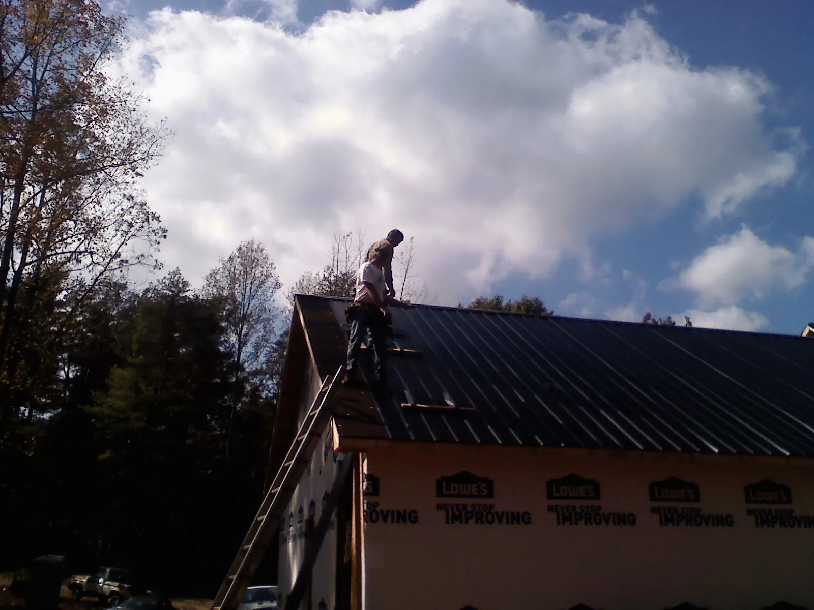 Roofer fastening dark metal panels high against a cloudy sky, from a Roof Inspection job in Gauley Bridge