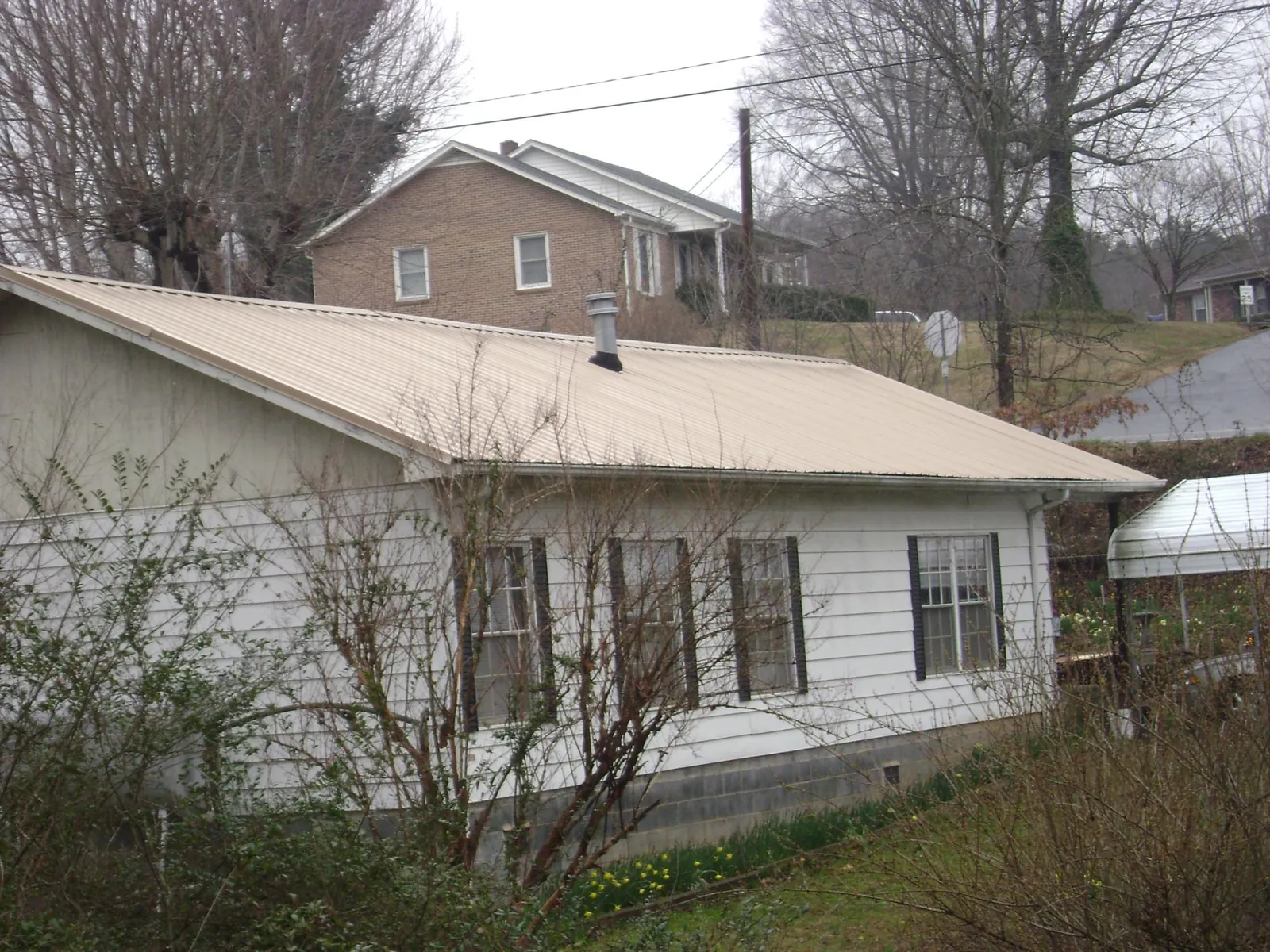 Tan metal roof on a white sided house set into a hillside — Commercial Roofing by Roofing Brothers in Gauley Bridge